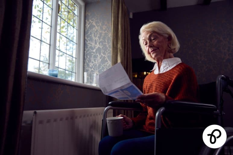 Older disabled woman in wheelchair reviewing an energy bill at home near a radiator, highlighting Priority Services Register UK support and accessible utility help for disabled households through Purpl discounts.
