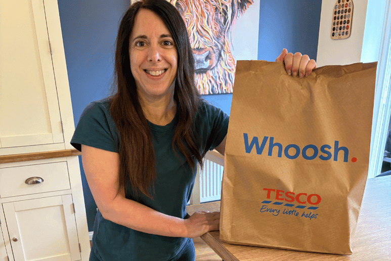 Georgina from Purpl holding a Tesco Whoosh delivery bag for an article about grocery delivery savings, disabilities and long-term health conditions with Purpl discounts.