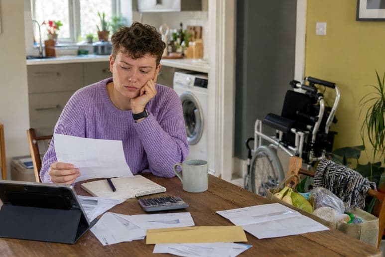 Disabled person reviewing household bills and local council support paperwork at home
