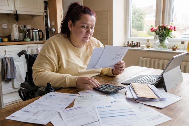 Disabled person reviewing energy, water and broadband bills at home while checking disability utility support options.