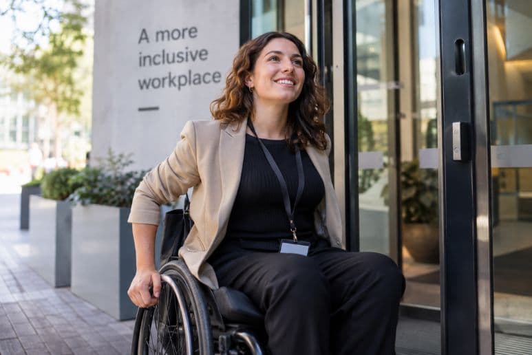 Disabled woman using a wheelchair arriving at work, showing how disability support can help people remain in employment.